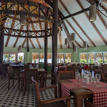 Impressive Punta Cana Hotel Exterior photo The photo shows the interior of a restaurant featuring a tropical or beachy design. The space has high, slanted ceilings with wooden beams and a large decorative light fixture. The floor is tiled in a black-and-white checker pattern. There are wooden