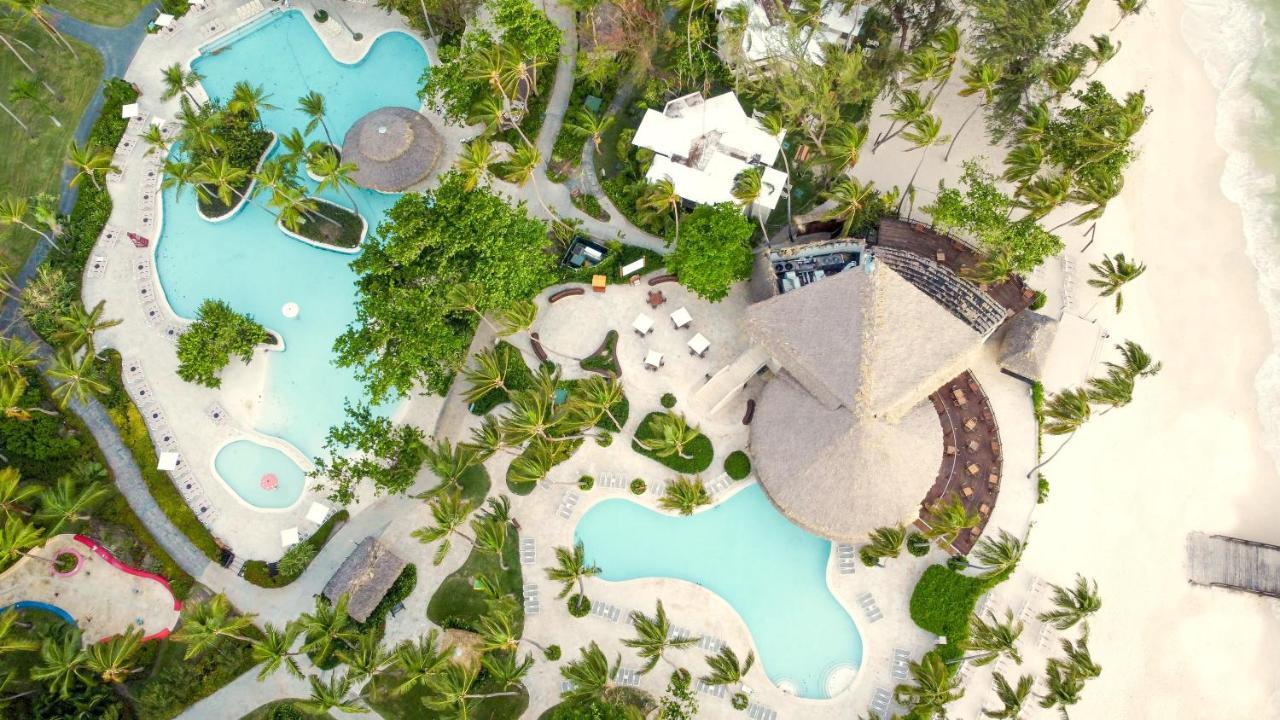 Impressive Punta Cana Hotel Exterior photo The photo shows an aerial view of a resort area featuring several swimming pools, surrounded by lush greenery and palm trees. There are smooth paths winding through the landscape, with lounge chairs placed around the pools. A thatched-roof structure 