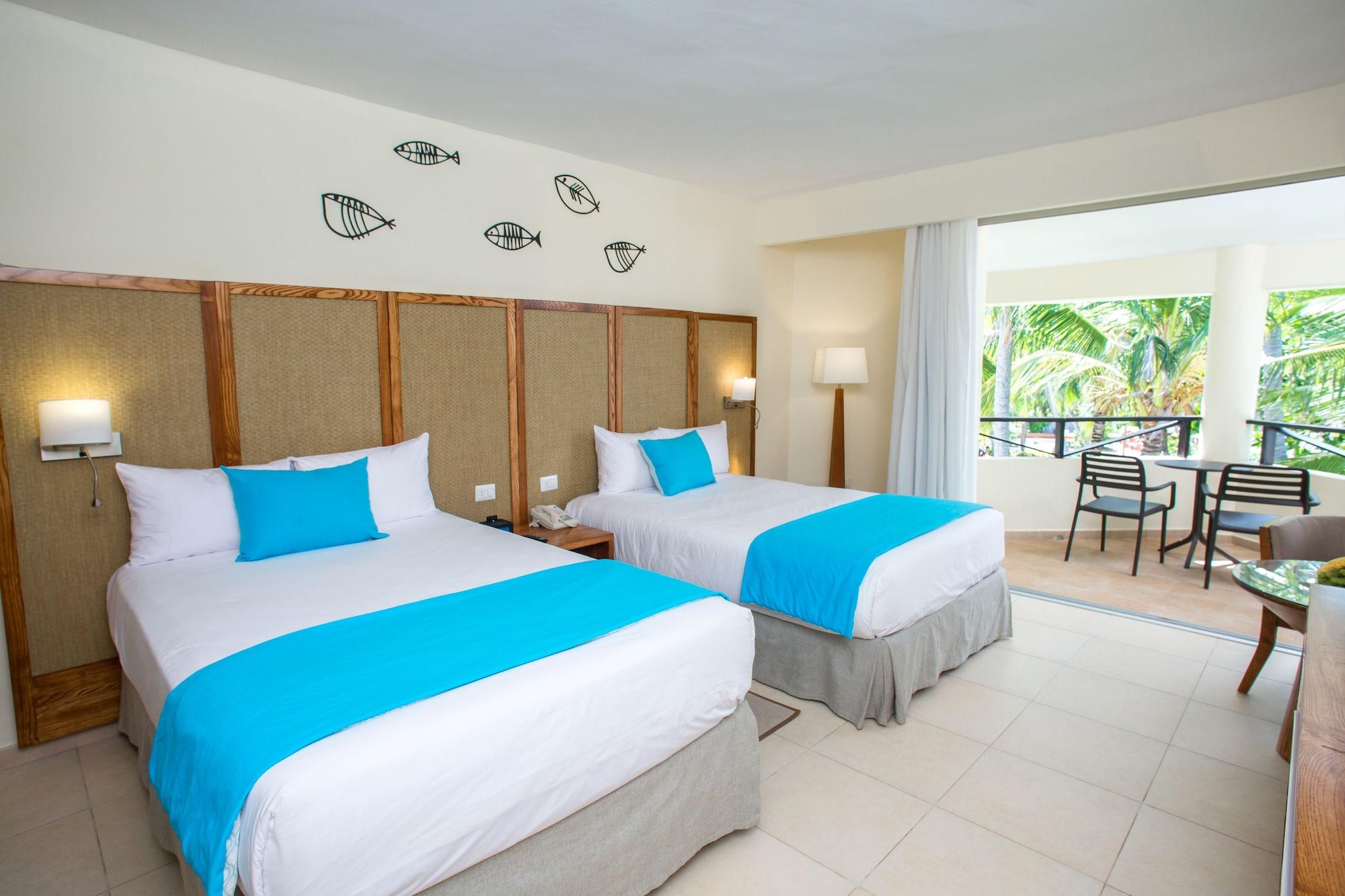 Impressive Punta Cana Hotel Exterior photo The photo shows a hotel room featuring two beds with white linens and bright turquoise decorative elements. The walls are light-colored, and there's a decorative pattern of fish above the beds. The room has a lamp beside one of the beds and a spaciou