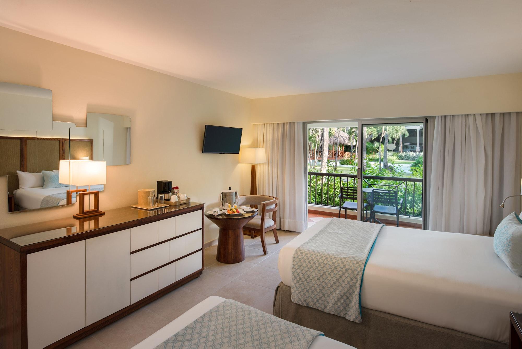 Impressive Punta Cana Hotel Exterior photo The photo depicts a cozy hotel room featuring two neatly made twin beds with light-colored bedspreads. A modern dresser with a flat-screen TV mounted on the wall is positioned across from the beds. There's a stylish bedside lamp and a small round tab