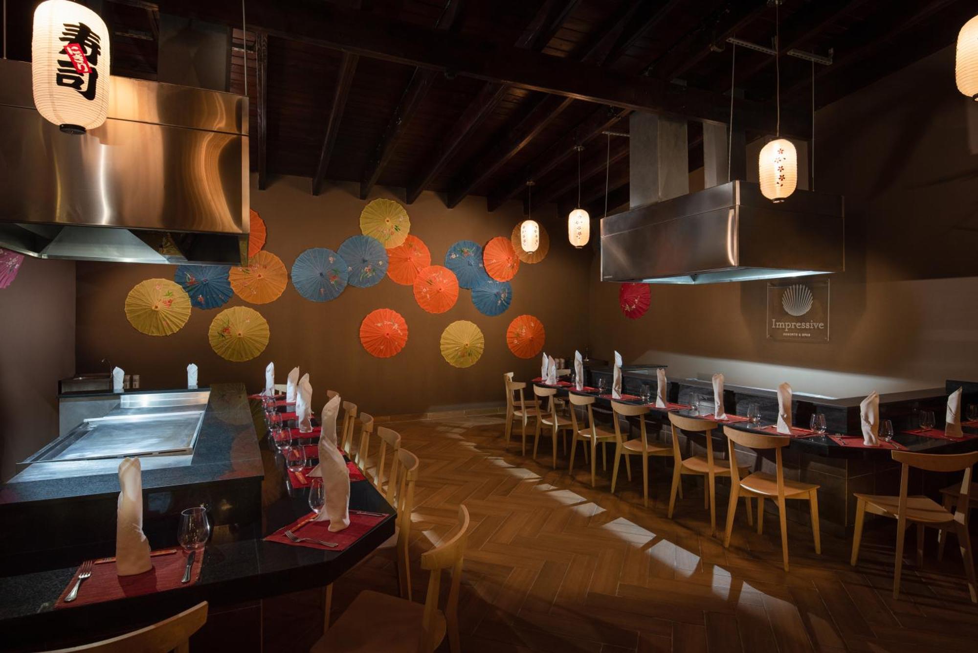 Impressive Punta Cana Hotel Exterior photo The photo depicts the interior of a restaurant. The decor features a minimalist design with wooden flooring and a long table arranged with chairs. The table appears to be set with napkins and glassware. In the background, there is a vibrant wall ador