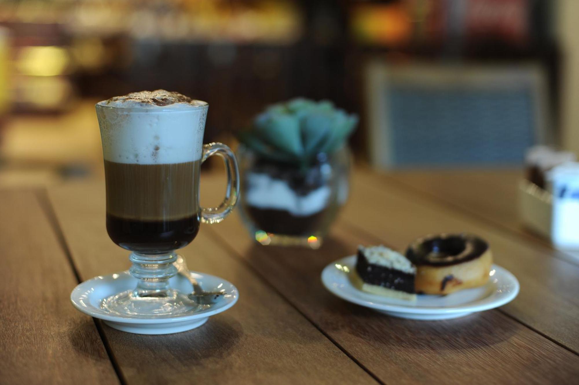 Impressive Punta Cana Hotel Exterior photo The photo shows a glass of layered coffee topped with foam and possibly cocoa powder, presented on a small white plate. Beside the coffee, there is a plate with two types of pastries: one appears to be a swirl-shaped pastry, likely cinnamon or chocol