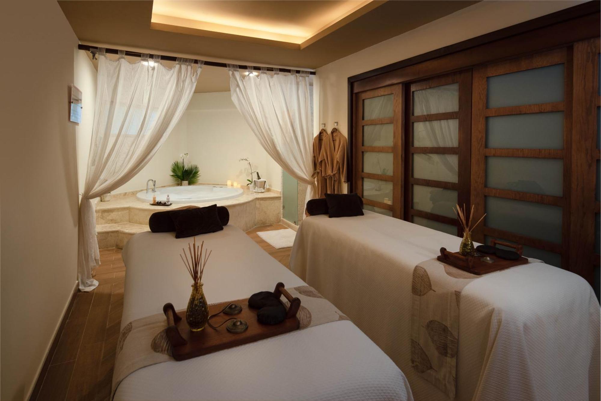 Impressive Punta Cana Hotel Exterior photo The photo shows a calming spa room designed for relaxation and wellness treatments. There are two massage tables covered with white linens, each featuring decorative items like small potted plants and stones on wooden trays. Sheer curtains provide a 