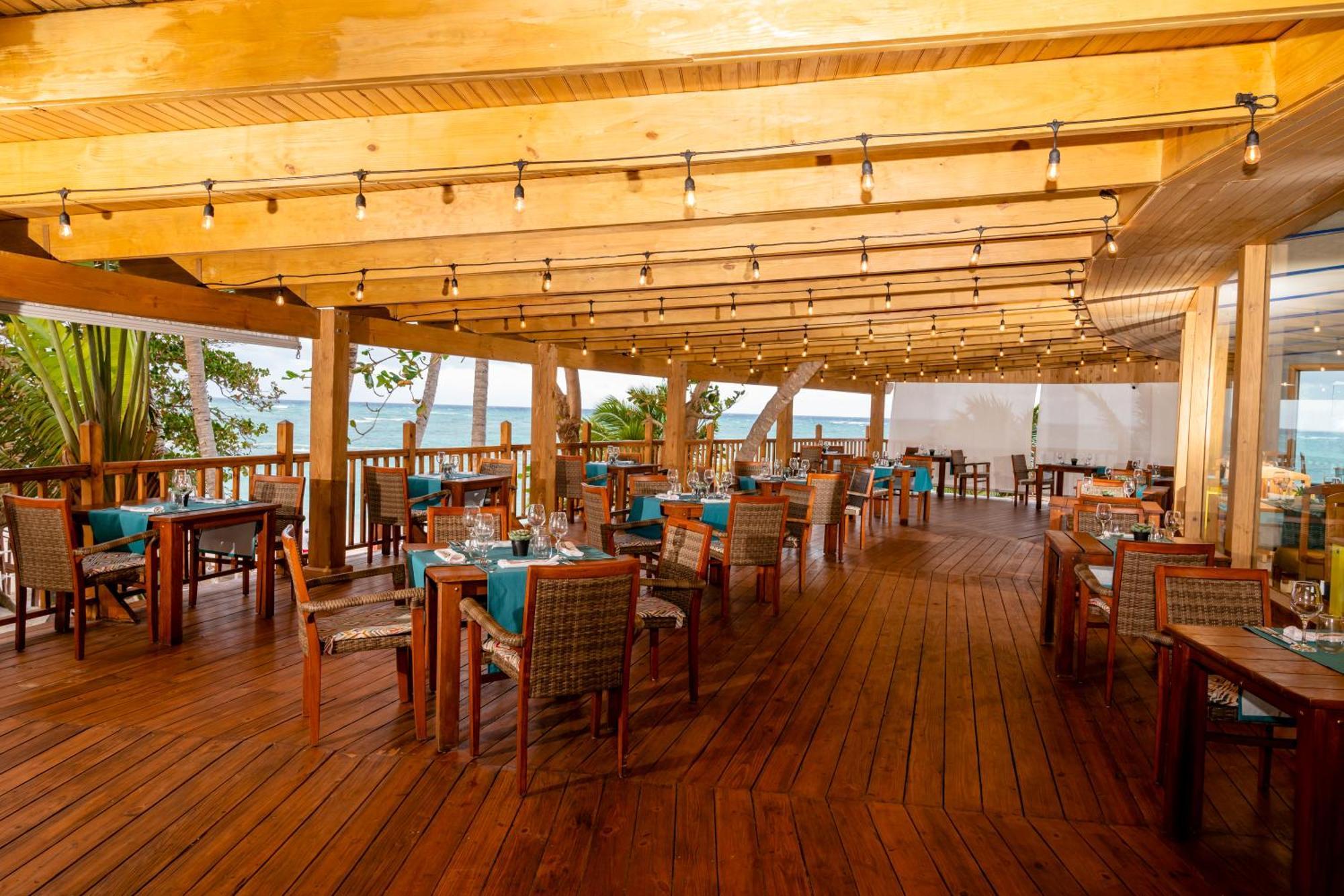 Impressive Punta Cana Hotel Exterior photo The photo shows the interior of a restaurant with a spacious and inviting atmosphere. The design features a wooden structure, with exposed beams and a polished wood floor. The tables are well-arranged, each adorned with blue tablecloths, and there ar