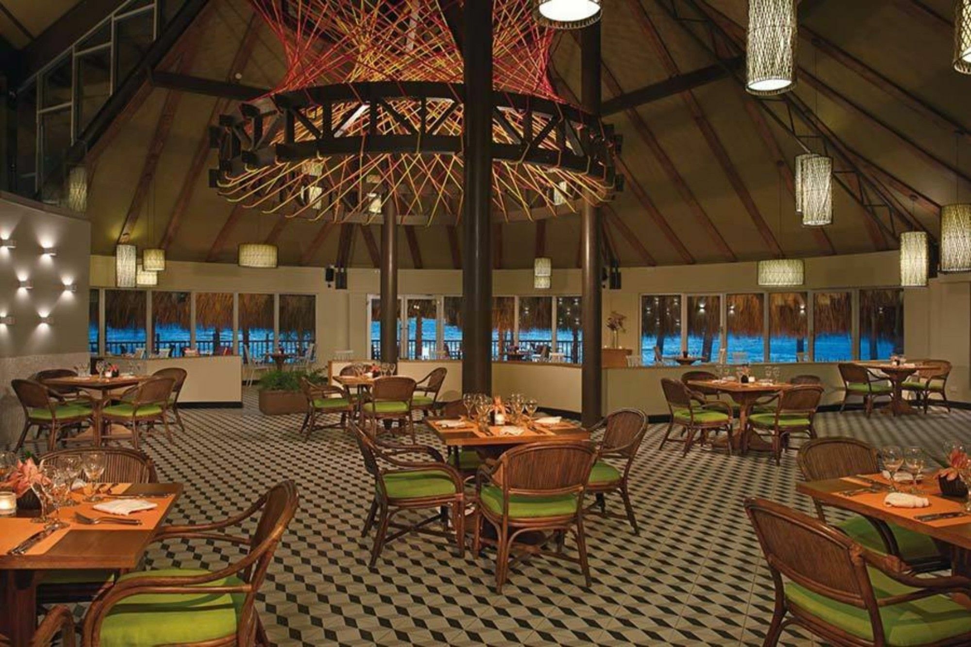 Impressive Punta Cana Hotel Exterior photo The photo shows a dining area in a restaurant with a modern and stylish design. The space features a high, vaulted ceiling supported by wooden beams, and a large, artistic chandelier hanging from the center. The floor has a distinctive black and whit