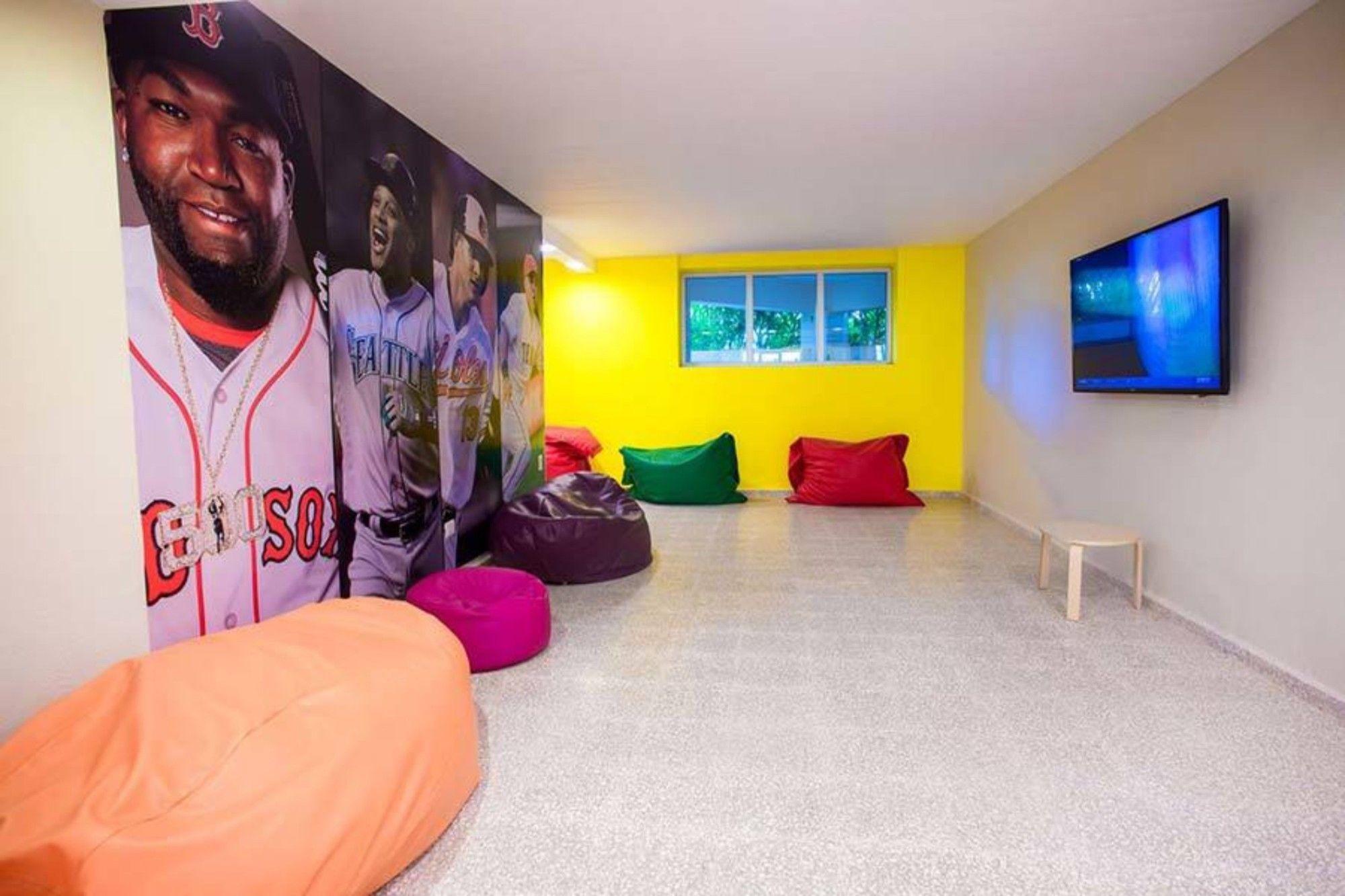 Impressive Punta Cana Hotel Exterior photo The photo shows a vibrant indoor space designed for relaxation or entertainment. The walls are painted in bright colors, including a cheerful yellow. One wall features large, colorful images of baseball players, while another wall has a flat-screen t