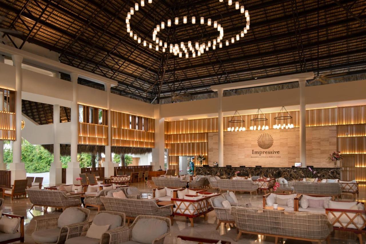 Impressive Punta Cana Hotel Exterior photo The photo depicts a spacious and elegantly designed interior of a restaurant or lounge area. The ceiling features a modern, circular chandelier with hanging lights, creating a warm ambiance. The walls are adorned with soft lighting and wood accents, 